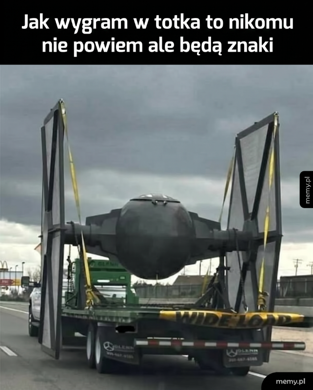 Czarny pojazd przypominający myśliwiec na przyczepie, z dużymi skrzydłami.