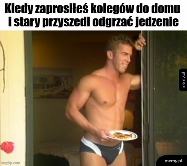 Mężczyzna w kąpielówkach trzyma talerz z jedzeniem, stojąc w drzwiach.