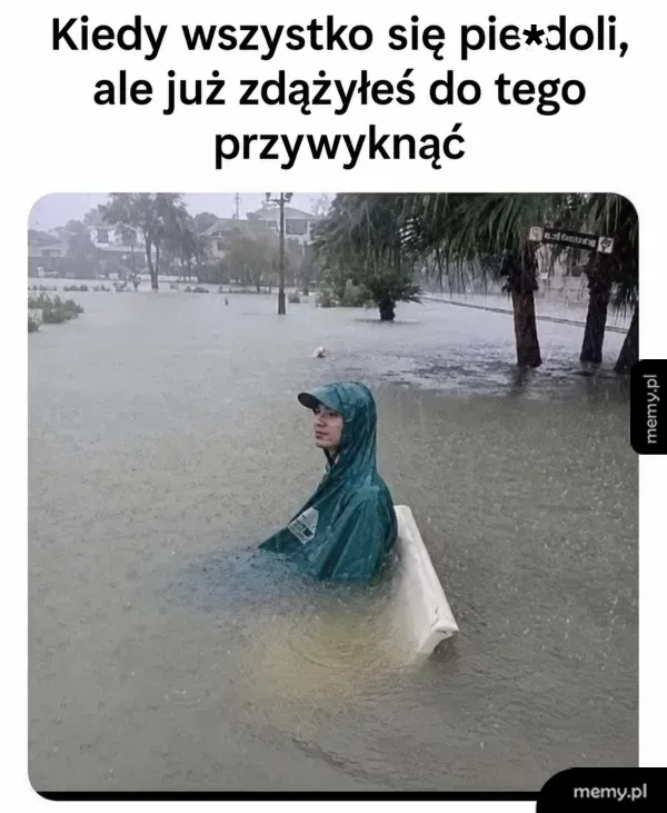 Osoba w wodzie, siedząca na desce w zalanym terenie.
