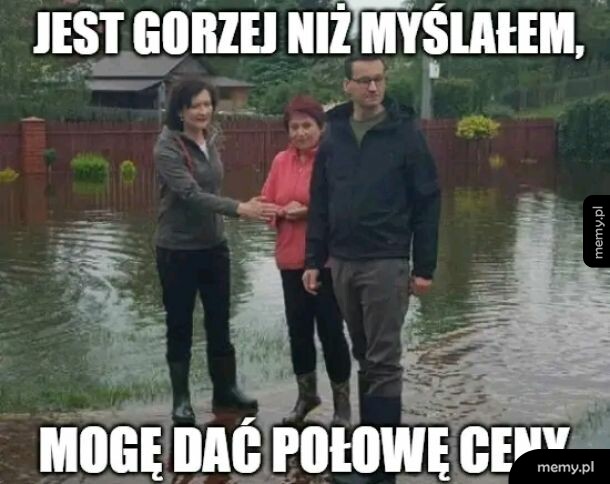 Mateusz Morawiecki i dwie kobiety stoją na zalanym terenie w kaloszach.