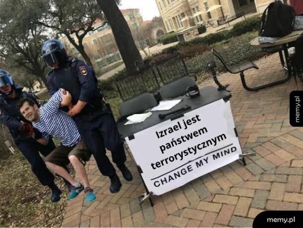 Policjanci wyprowadzają mężczyznę siedzącego przy stoliku z kontrowersyjnym transparentem.