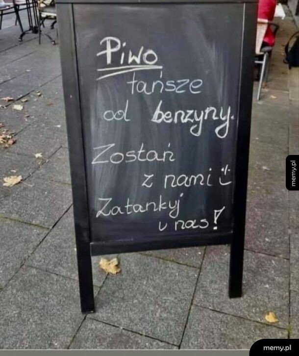 Czarna tablica kredowa z napisem o piwie i benzynie stojąca na chodniku.