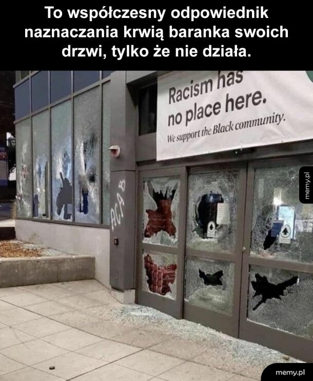 Zniszczony budynek z banerem antyrasistowskim i powybijanymi szybami.